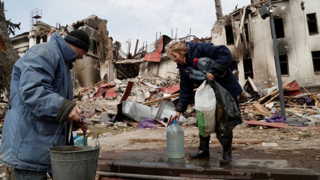Local residents draw water from a well near the building of a destroyed theatre in Mariupol