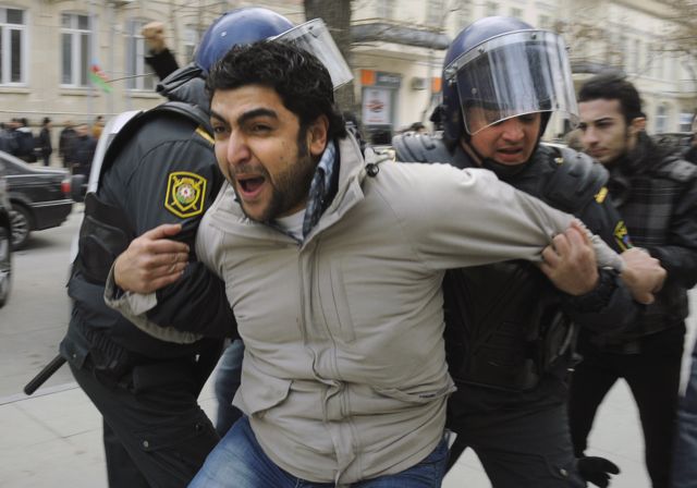 Двое полицейских задерживают молодого человека на митинге оппозиции