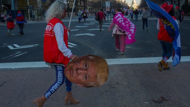 Женщина с флагом несет картонное лицо Трампа