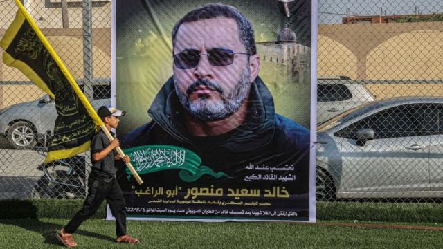 Палестинский мальчик с флагом "Исламского джихада" проходит мимо фотографии лидера группировки Халеда Мансура