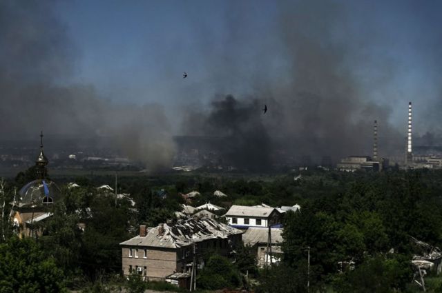 A damaged building is pictured in Lysychansk as black smoke and dirt rise from the nearby city of Severodonetsk during battle between Russian and Ukrainian troops in the eastern Ukraine region of Donbas on June 9, 2022