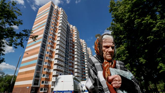 Пожилая москвичка на фоне пострадавшего дома