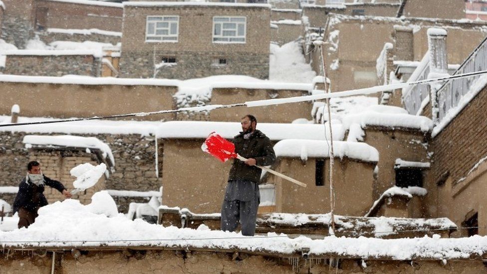 Afghan youth shovel snow from the roof of houses in Kabul