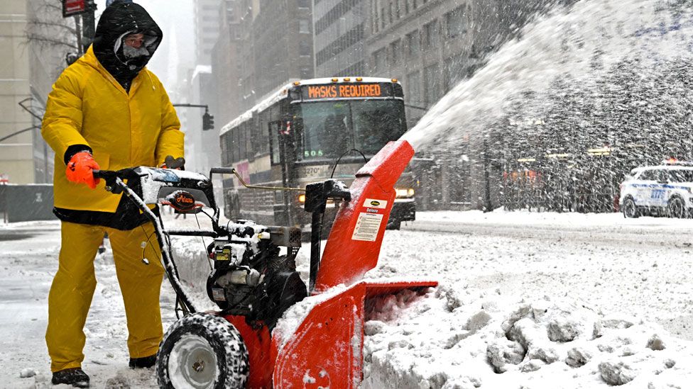 A worker uses a snow blower to clear snow as the wind carries it on 29 January 2022 in New York City
