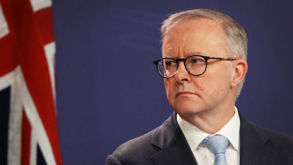 Anthony Albanese in front of a blue background and the Australian flag