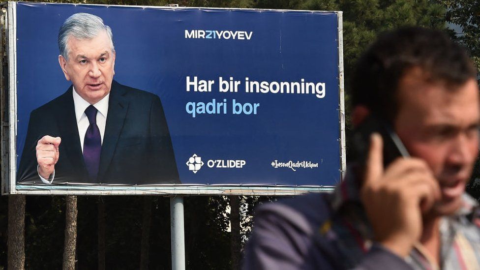 A man talks on a mobile phone in front of a campaign billboard of Uzbekistan's President and presidential candidate Shavkat Mirziyoyev