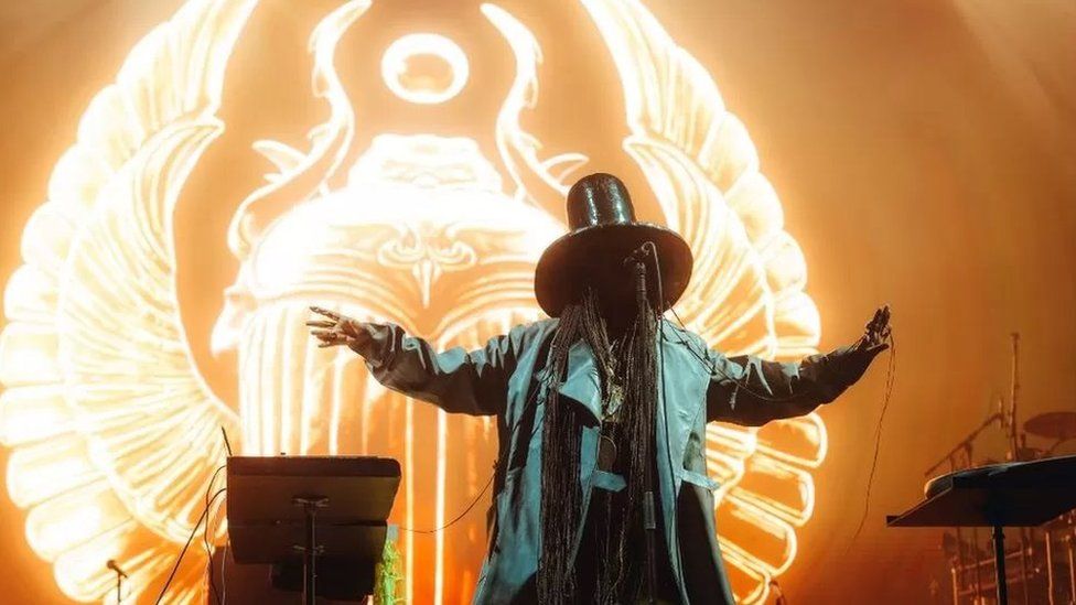 Erykah Badu singing in front of an orange backdrop