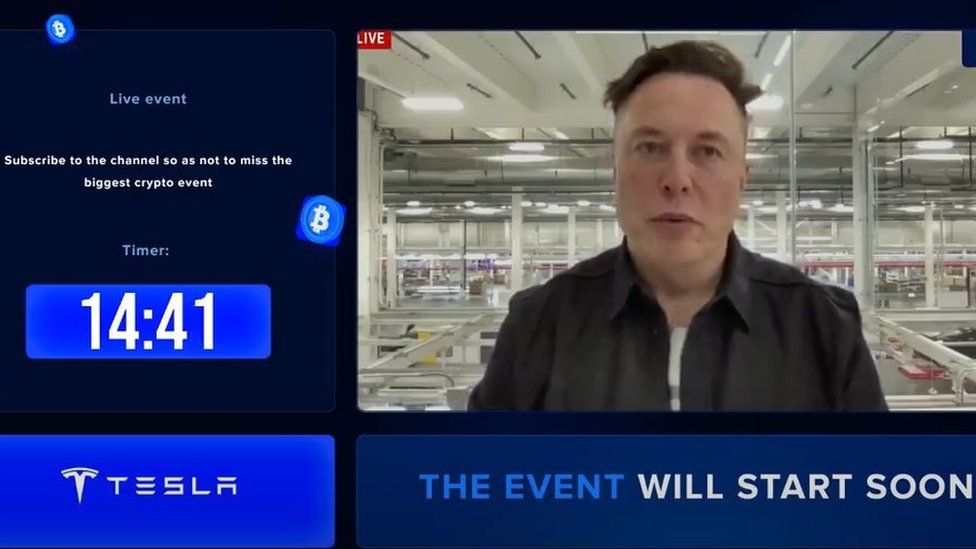 A still taken from a YouTube video. It shows Elon Musk along with text such as "the event will start soon" and "Tesla".