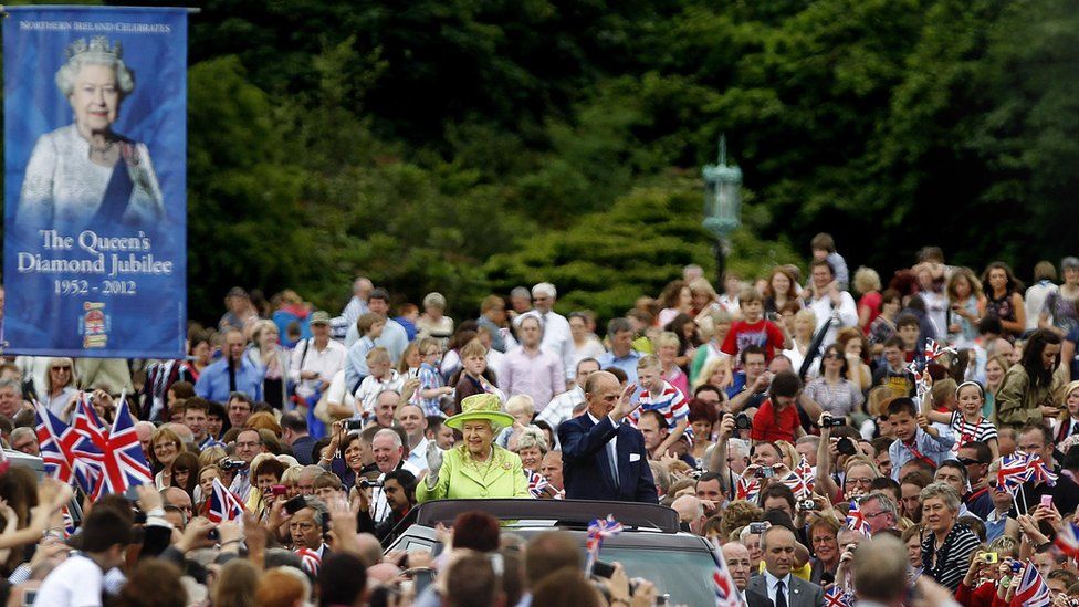 The Queen and Prince Phillip waving from a car amidst crowds