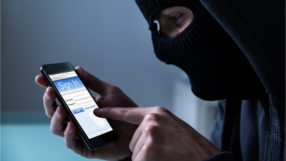 Hooded hacker stealing data on smartphone