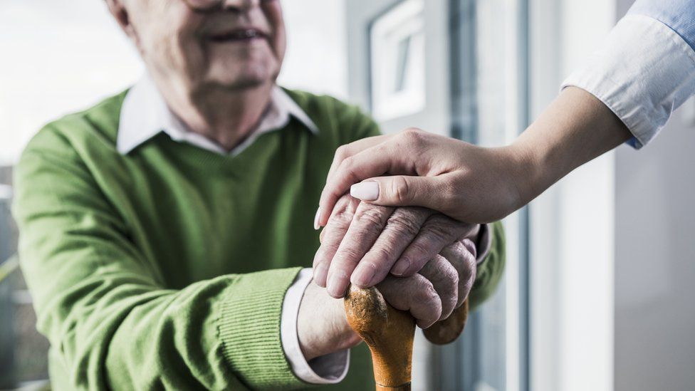 A woman placing her hand on those of an elderly man