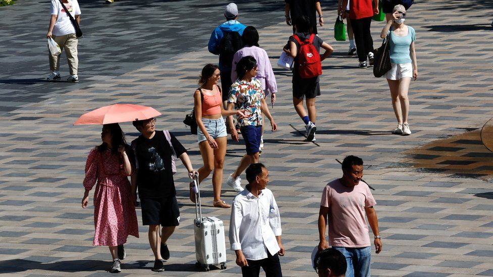 People hold umbrellas and shield their face from the sun while walking through a shopping square in Beijing on 22 June