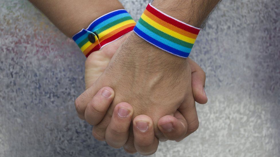 Men holding hands with rainbow bracelets on