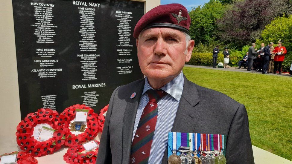 Platoon Sgt Manny Manfred with medals on his chest standing in front of Falklands memorial stone
