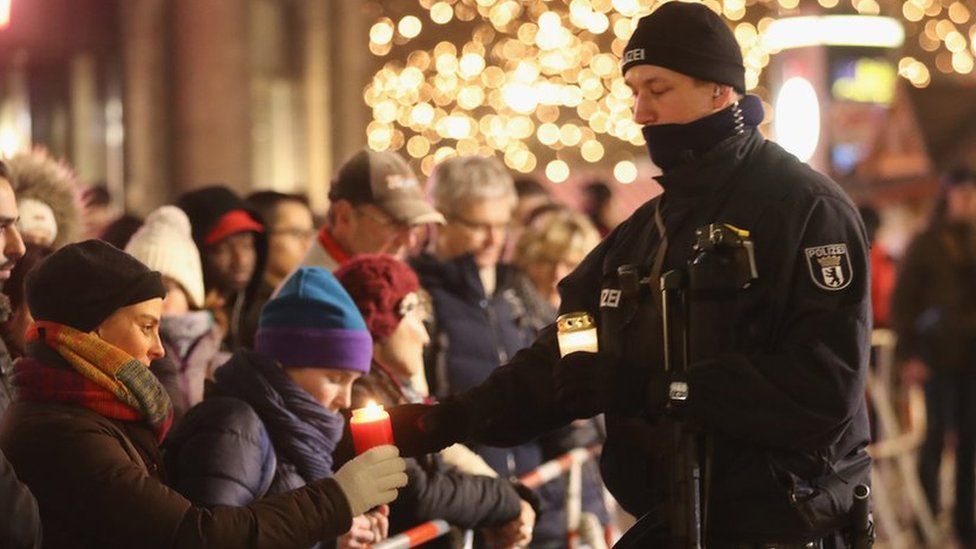 A policeman takes a candle from a mourner to place it at a makeshift memorial in Berlin