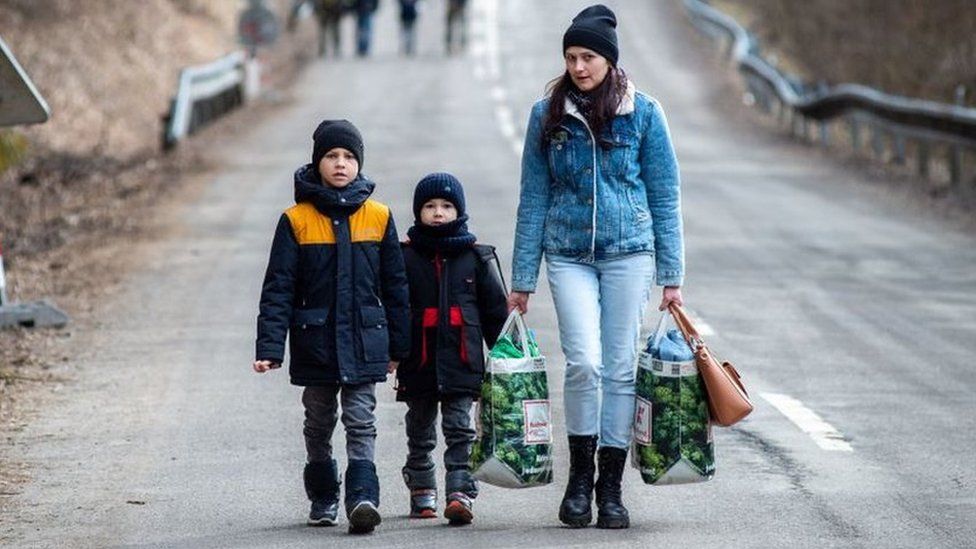 A woman with two children and carrying bags walk on a street to leave Ukraine after crossing the Slovak-Ukrainian border