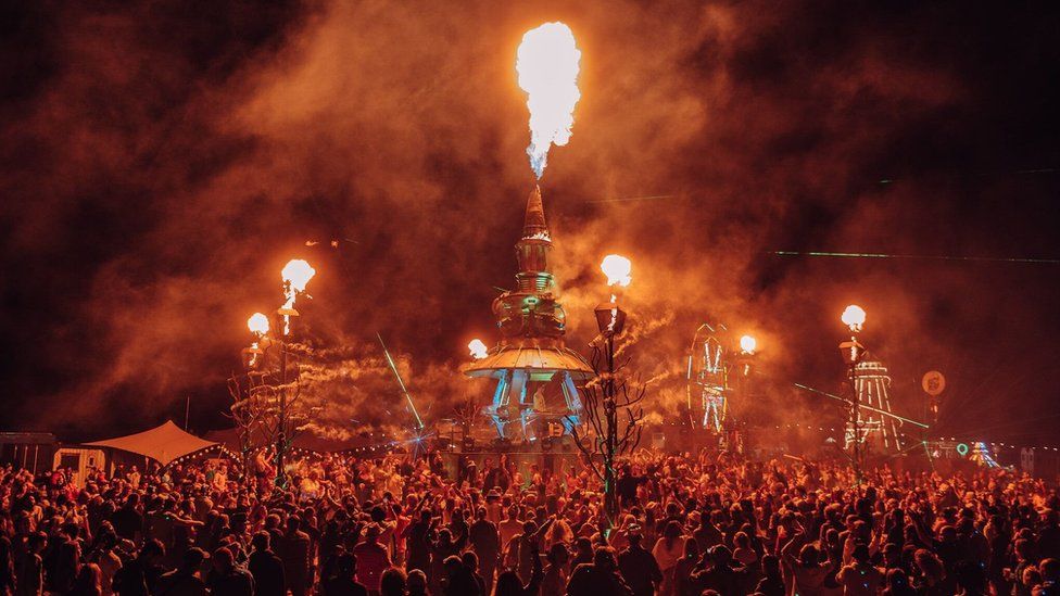 A crowd watching a performance on Arcadia with fire coming out of it at three points