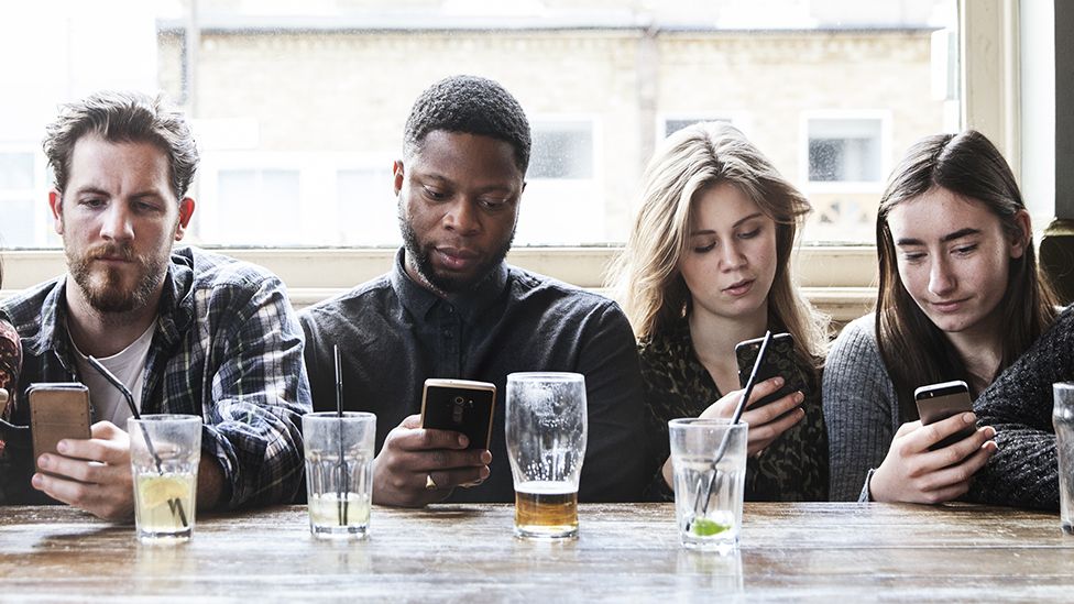 A group of people in a pub all looking at their phones (stock photograph)