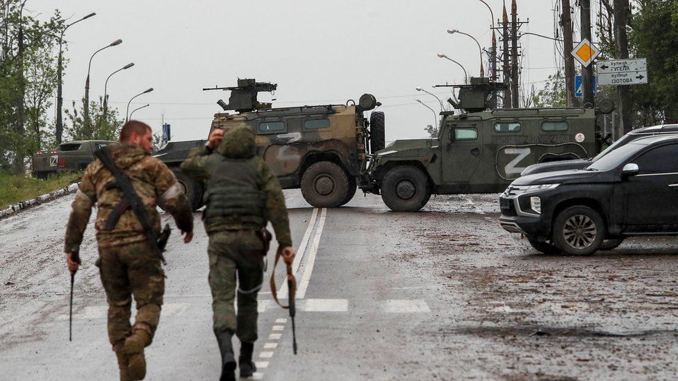 Two Russian soldiers walk towards armoured cars