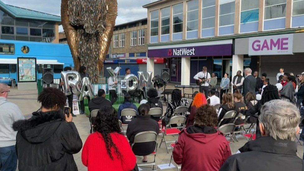 People gather round a statue made of thousands of knives in a town square