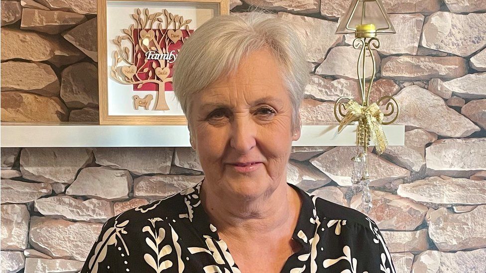 Wendy Falconer standing in a living room. She is middle-aged, with short blonde hair.