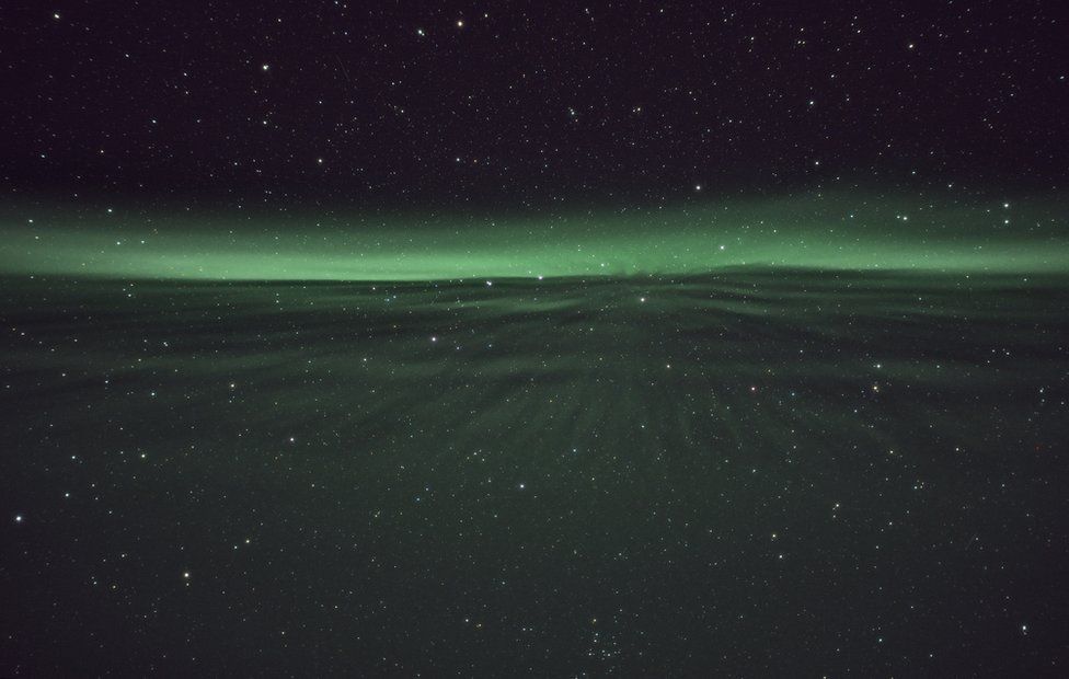 A shimmering green sheet reaches through a sky of stars towards a glowing green horizon