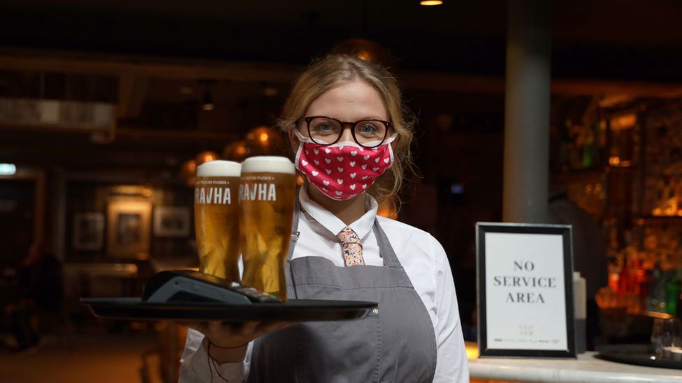 A waitress wearing a mask carried a tray of beers