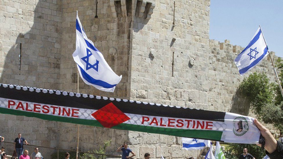Israel flags flying and a Palestinian scarf with "Palestine" written on it