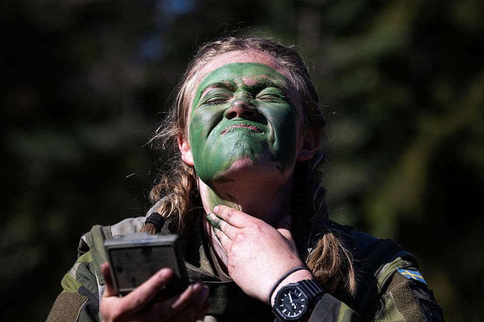 A soldier of the P18 Gotland Regiment covers her face with paint during a field exercise near Visby on the Swedish island of Gotland