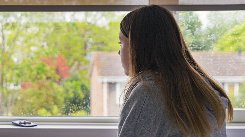 Stock image of a teenage girl looking out of a bedroom window