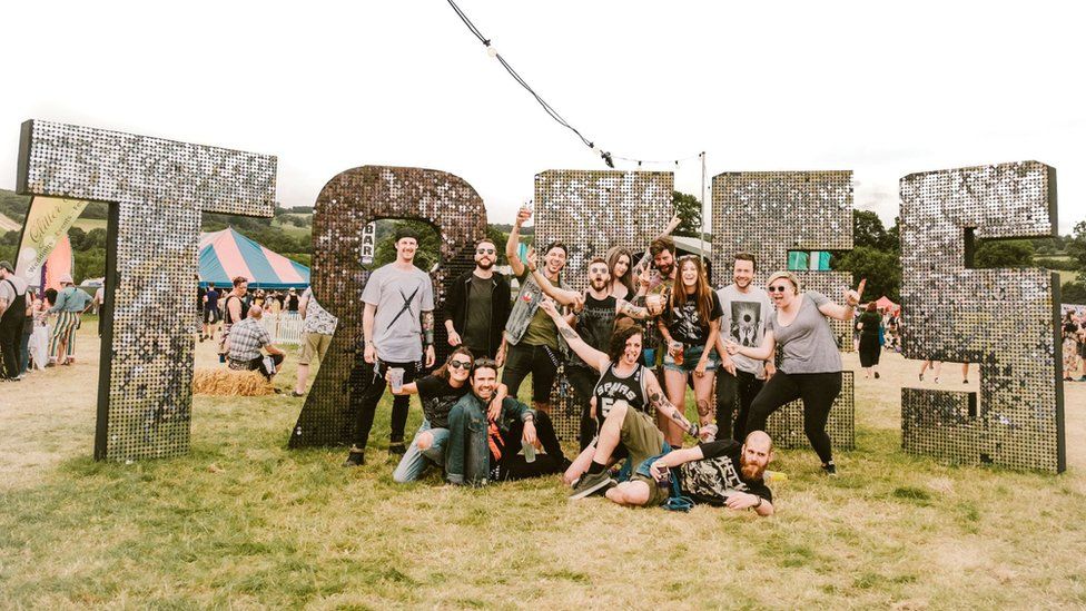 A group of people posing in front of a big silver, glittery 'Trees' sign