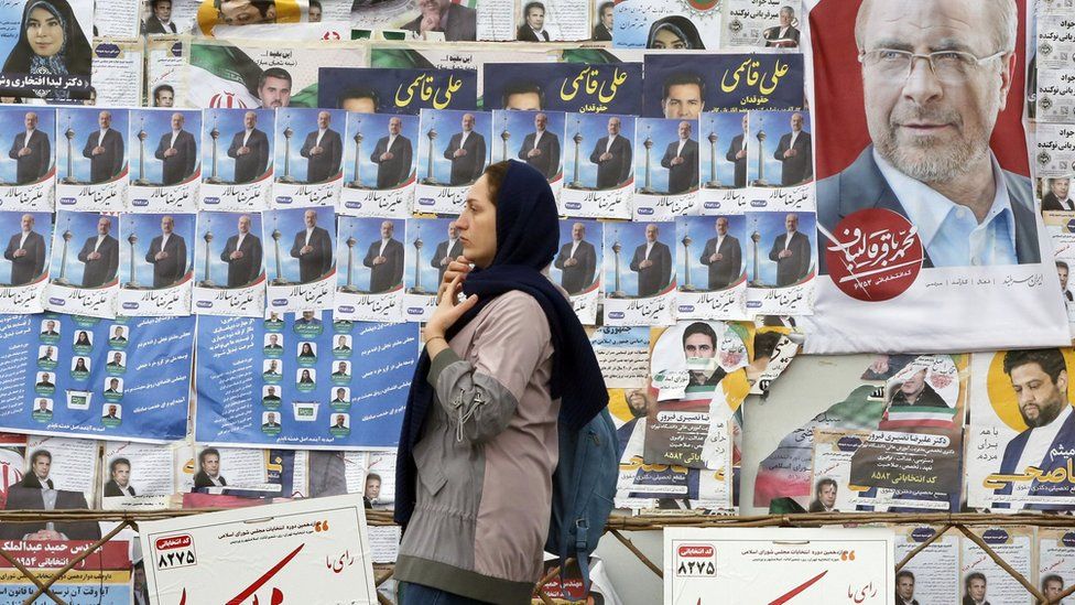 File photo showing a woman walking past electoral posters in Tehran, Iran (28 February 2024)
