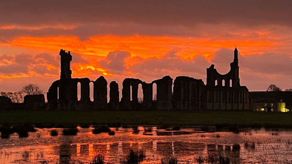 A bright orange sunset over a body of water, with old ruins in the background