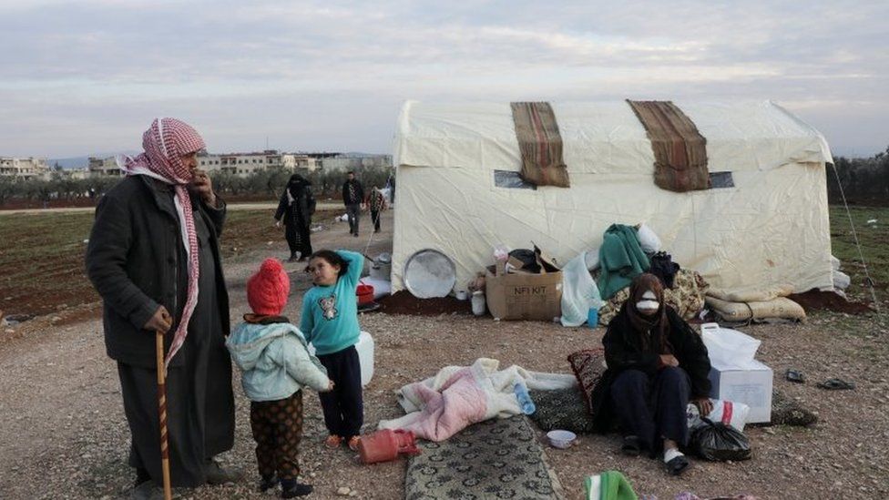 Earthquake survivor, Mahmoud Abd el-Shehiel, stands with his children outside tents erected for people affected by a devastating earthquake, in rebel-held town of Jandaris, Syria