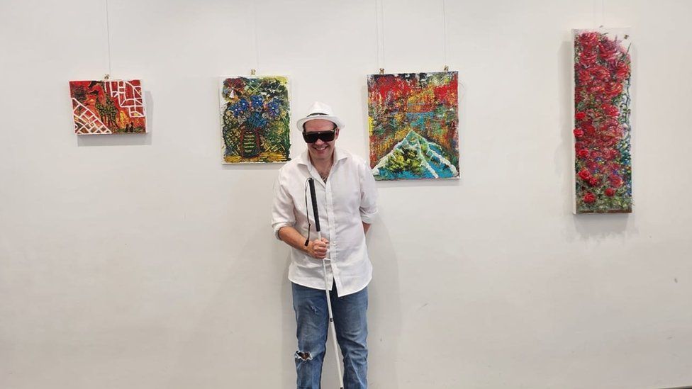 Adrian Paternoster stood in front of some of his artwork hanging at a gallery