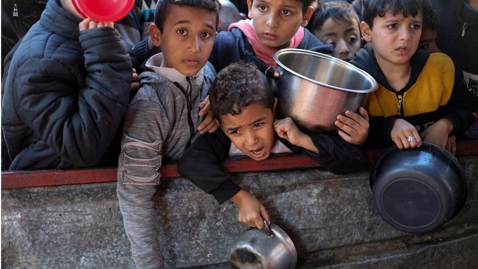 Palestinian children wait to receive food cooked by a charity kitchen in Rafah, southern Gaza