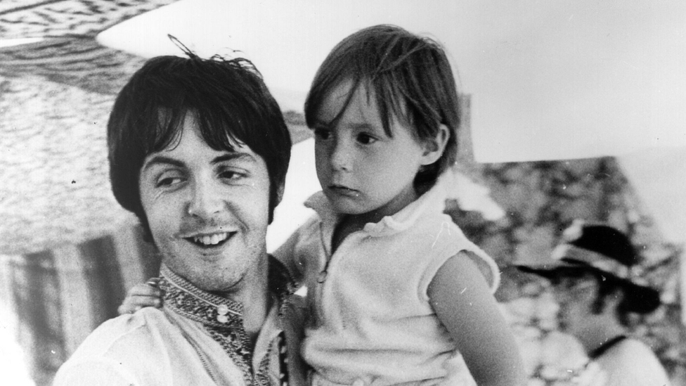 Paul McCartney holds four year old Julian, son of his colleague John Lennon (visible in the background) during a holiday