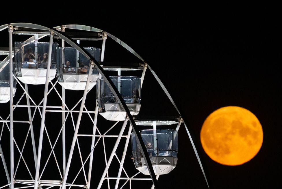 The August full moon rises behind the ferris wheel at Bristol International Balloon Fiesta