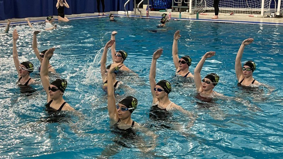 Artistic swimmers performing a routine in a swimming pool