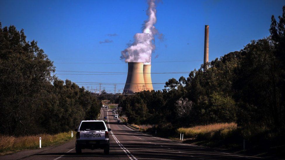 A car drives towards smoke and steam rising from the Bayswater coal-powered thermal power station located near the central New South Wales town of Muswellbrook, New South Wales, Australia