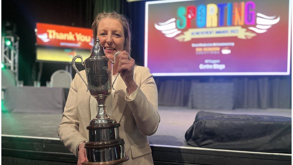 Alex Scott's mum, Stephanie Allen, holding a trophy.