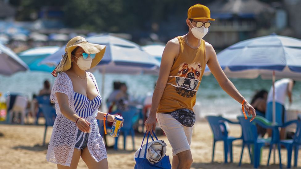 Tourists wearing a mask walk along Caleta beach on March 19 2021 in Acapulco, Mexico