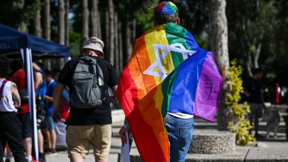 A man carries a rainbow flag with the Star of David emblazoned on it
