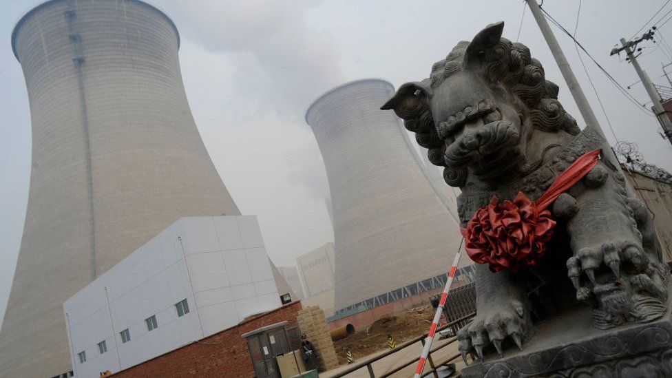 A security guard stands outside the cooling towers for a coal-powered power plant