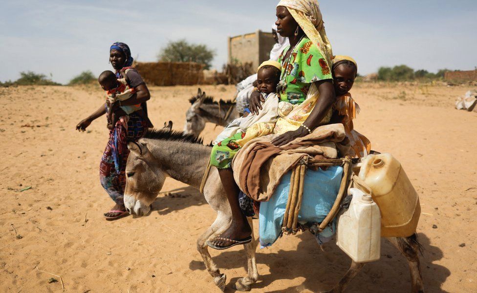 Displaced women and children in Darfur carry their belongings, assisted by donkeys