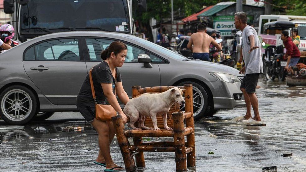 A woman moves her dog while residents evacuate from their submerged homes in the aftermath of Super Typhoon Noru in San Ildefonso, Bulacan province on September 26, 2022.