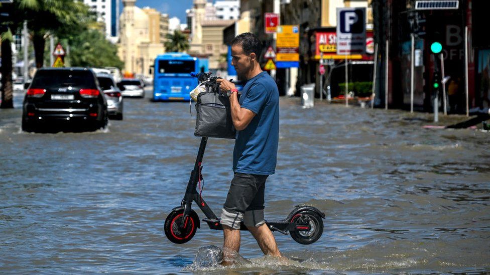 Man carrying a scooter with water up to his knees in Dubai