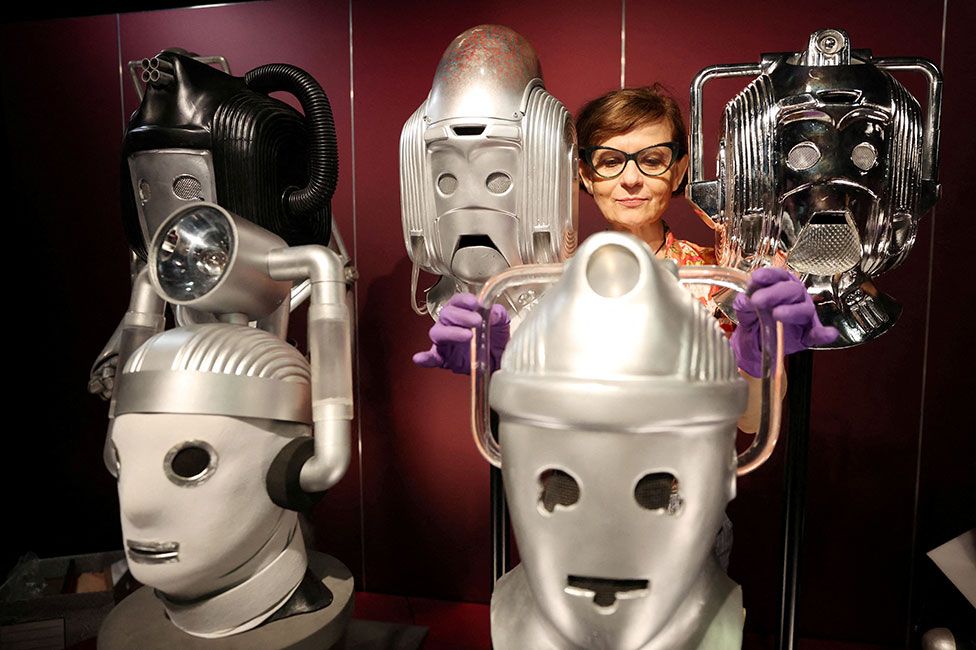 A sculpture conservator adjusts a display of cybermen heads at the Doctor Who Worlds of Wonder exhibition at the World Museum in Liverpool, UK