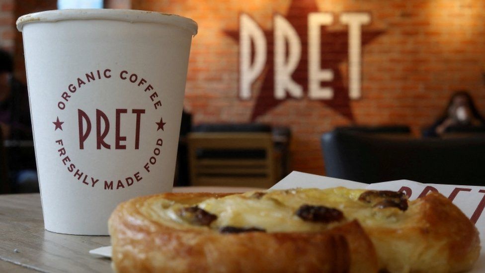 A coffee and a pastry are seen on a table inside a Pret A Manger store.