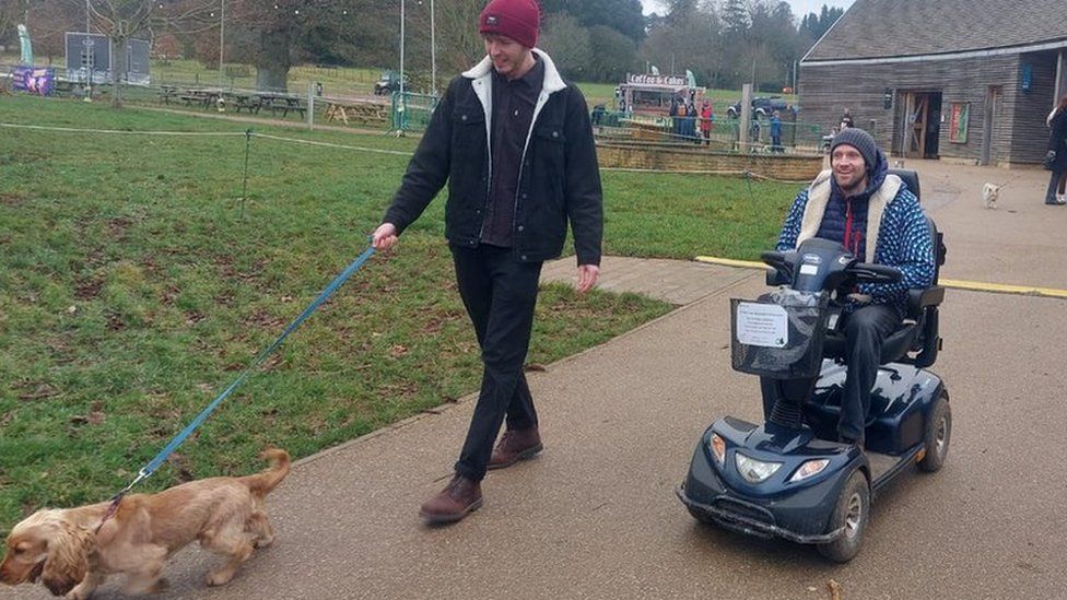 Two men, one in a mobility scooter, walking a dog